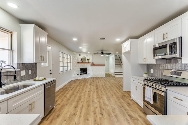 kitchen with sink, a brick fireplace, white cabinets, and appliances with stainless steel finishes