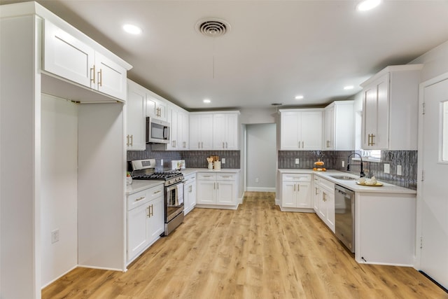 kitchen featuring tasteful backsplash, sink, white cabinets, stainless steel appliances, and light wood-type flooring