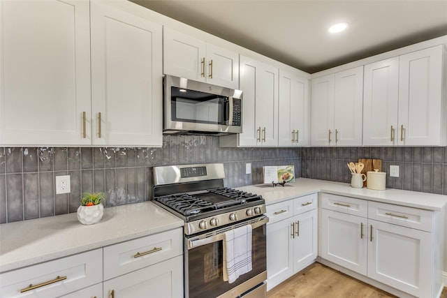 kitchen featuring white cabinetry, light stone counters, light hardwood / wood-style flooring, stainless steel appliances, and decorative backsplash