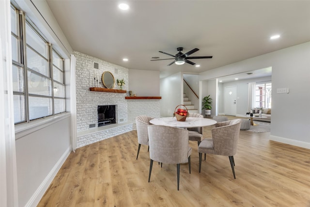 dining room featuring a brick fireplace, light hardwood / wood-style flooring, and ceiling fan