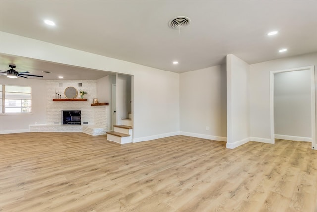 unfurnished living room with ceiling fan, a brick fireplace, and light hardwood / wood-style floors