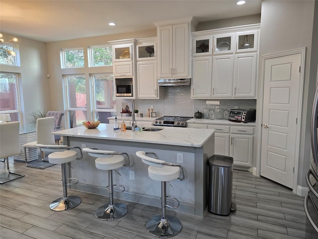 kitchen featuring sink, stainless steel appliances, backsplash, an island with sink, and white cabinets