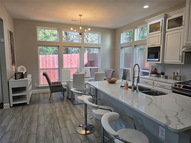 kitchen featuring white cabinetry, sink, hanging light fixtures, hardwood / wood-style flooring, and light stone countertops