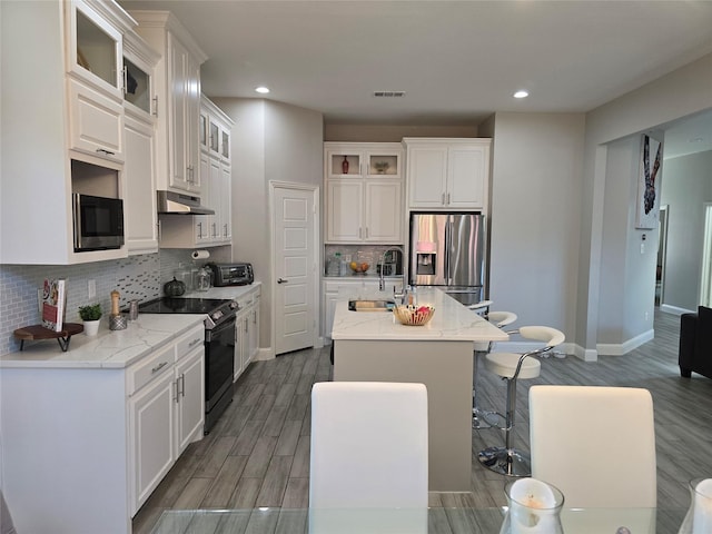 kitchen featuring white cabinetry, black range with electric stovetop, stainless steel fridge, and an island with sink