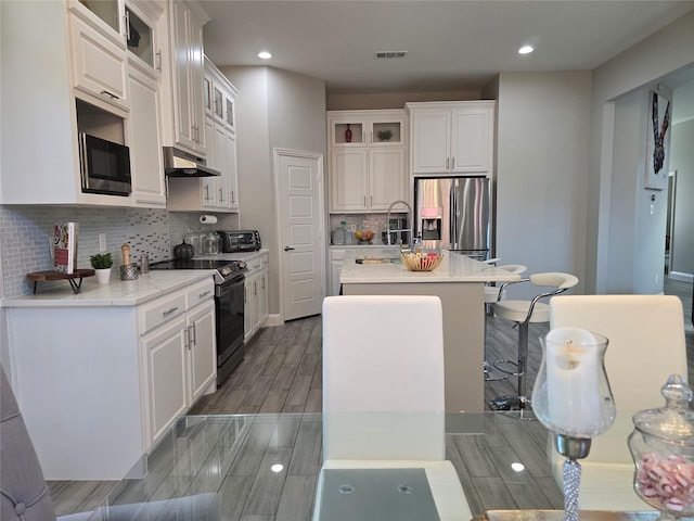 kitchen featuring built in microwave, white cabinetry, stainless steel refrigerator with ice dispenser, a center island with sink, and black / electric stove