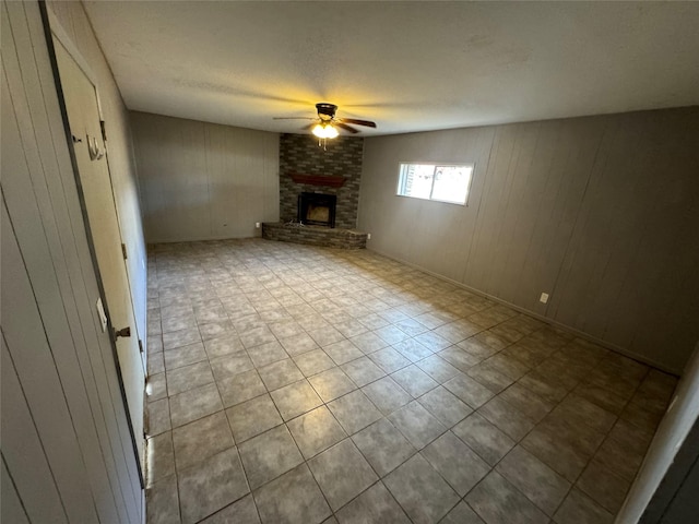 unfurnished living room with ceiling fan, wooden walls, a textured ceiling, and a brick fireplace