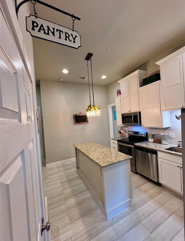 kitchen with appliances with stainless steel finishes, a center island, white cabinets, and decorative light fixtures