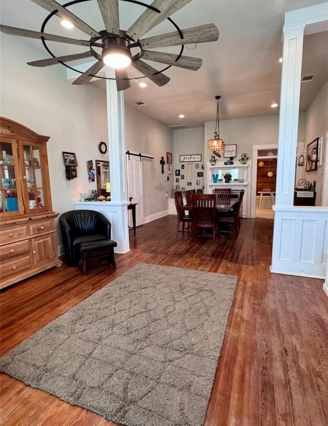 dining room featuring dark hardwood / wood-style flooring, a barn door, ceiling fan, and ornate columns