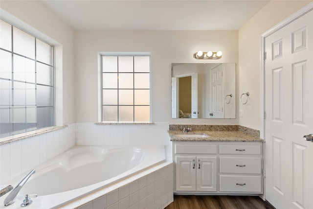 bathroom with vanity, tiled bath, a wealth of natural light, and hardwood / wood-style flooring