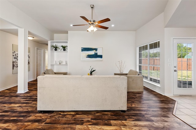 living room with built in shelves, dark hardwood / wood-style floors, a wealth of natural light, and ceiling fan