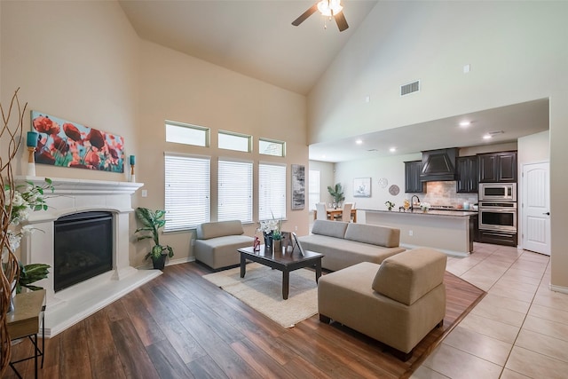 living room featuring ceiling fan, sink, high vaulted ceiling, and light hardwood / wood-style floors