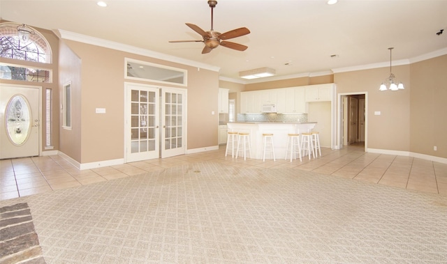 unfurnished living room with light tile patterned flooring, crown molding, ceiling fan with notable chandelier, and french doors