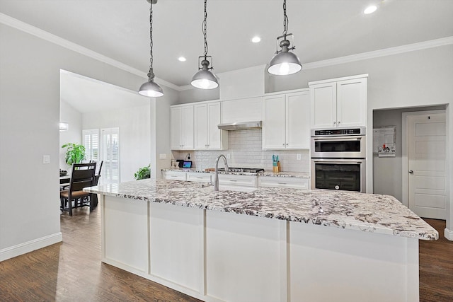 kitchen featuring white cabinets, a center island with sink, hanging light fixtures, appliances with stainless steel finishes, and tasteful backsplash