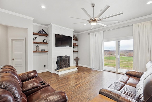 living room with dark wood-type flooring, ceiling fan, a large fireplace, and crown molding