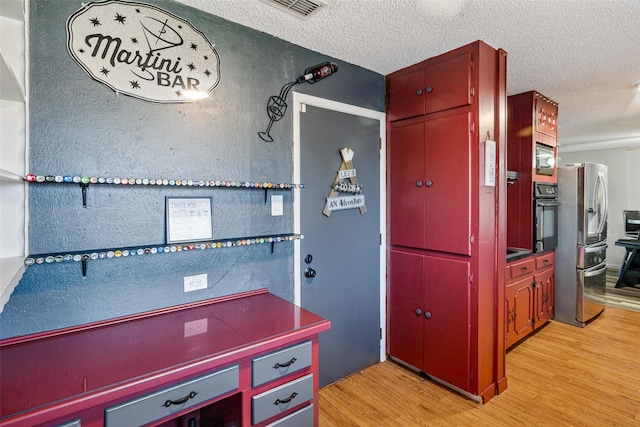 kitchen featuring built in microwave, stainless steel fridge, light hardwood / wood-style floors, a textured ceiling, and black oven