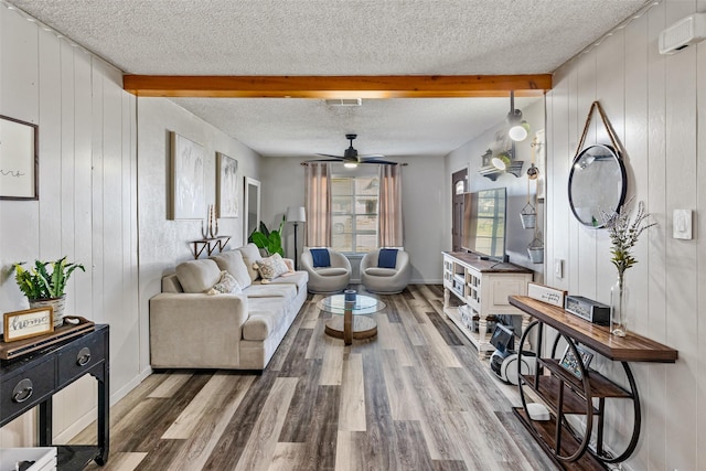 living room featuring beamed ceiling, ceiling fan, wood-type flooring, and wooden walls