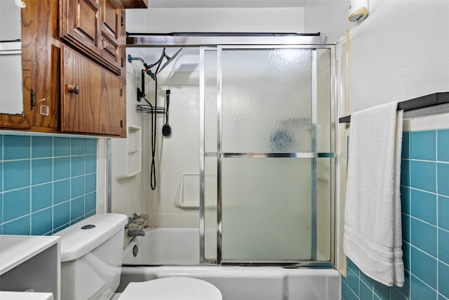 bathroom featuring shower / bath combination with glass door, toilet, and tile walls