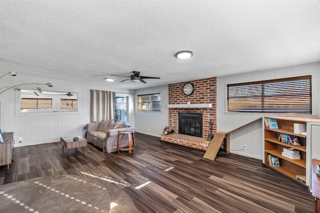 living room with a textured ceiling, ceiling fan, wooden walls, a fireplace, and dark hardwood / wood-style floors