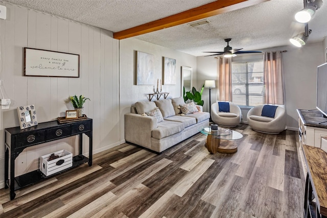 living room featuring a textured ceiling, ceiling fan, dark wood-type flooring, beamed ceiling, and wood walls