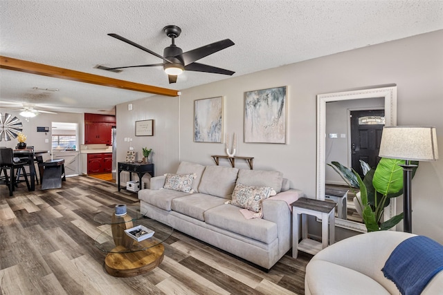 living room with ceiling fan, beamed ceiling, wood-type flooring, and a textured ceiling