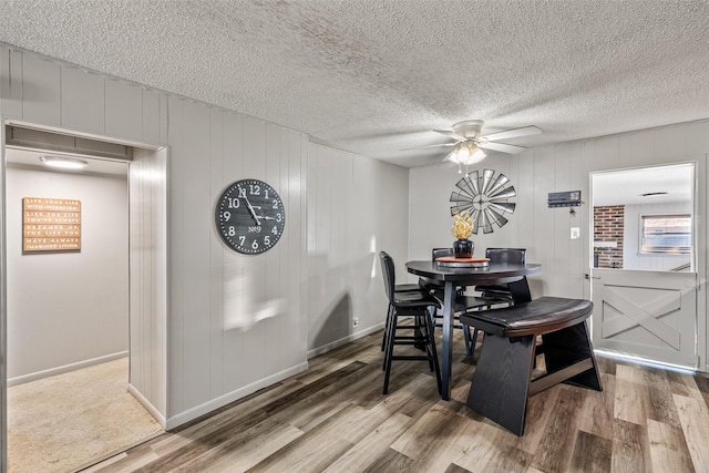 dining space with hardwood / wood-style floors, ceiling fan, a textured ceiling, and wooden walls