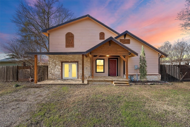 view of front of home with stone siding, fence, a lawn, and french doors