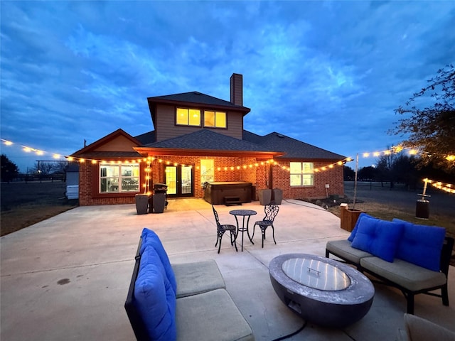 back house at dusk with an outdoor living space with a fire pit, a hot tub, and a patio