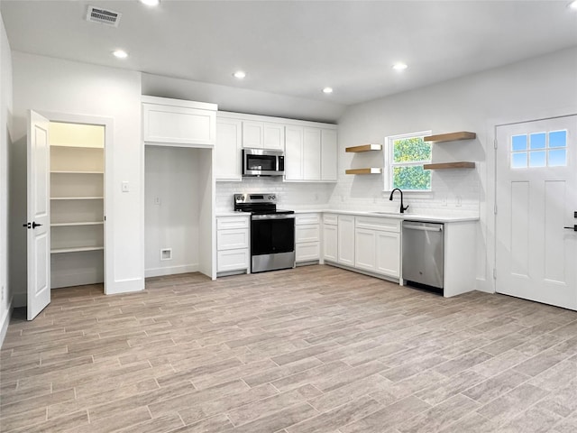 kitchen featuring appliances with stainless steel finishes, backsplash, sink, light hardwood / wood-style floors, and white cabinetry