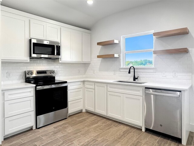 kitchen with sink, vaulted ceiling, tasteful backsplash, white cabinetry, and stainless steel appliances