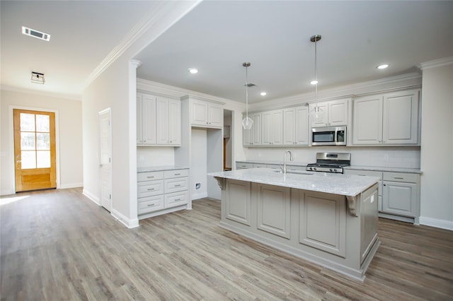 kitchen featuring an island with sink, sink, hanging light fixtures, stainless steel appliances, and light stone countertops