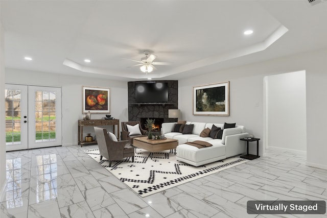 living room featuring french doors, a fireplace, a tray ceiling, and ceiling fan