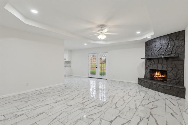 unfurnished living room with french doors, ceiling fan, a fireplace, and a tray ceiling