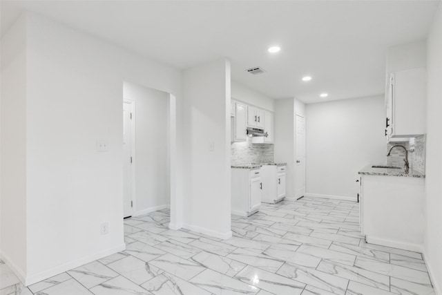 kitchen with light stone counters, sink, decorative backsplash, and white cabinets