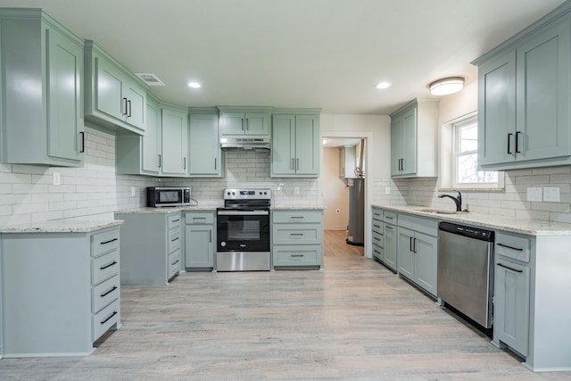 kitchen featuring sink, light stone counters, light wood-type flooring, stainless steel appliances, and decorative backsplash