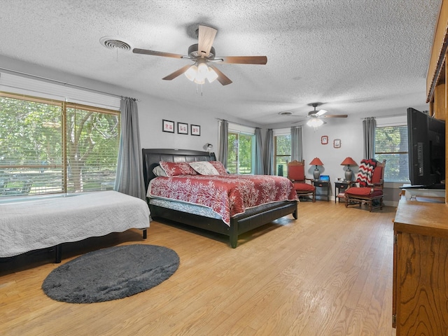 bedroom with multiple windows, ceiling fan, a textured ceiling, and light hardwood / wood-style floors