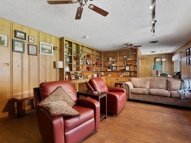 living room with wood-type flooring, wooden walls, ceiling fan, and a textured ceiling