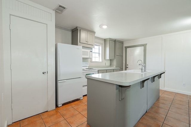 kitchen with light tile patterned floors, white appliances, gray cabinets, and an island with sink