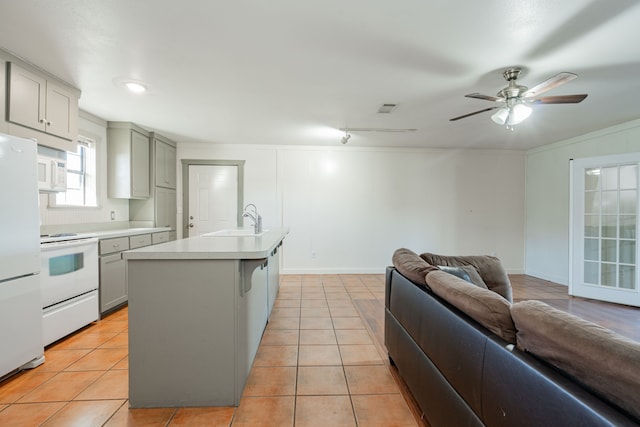 kitchen with sink, white appliances, gray cabinets, an island with sink, and light tile patterned flooring