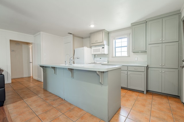 kitchen featuring an island with sink, a kitchen bar, light tile patterned floors, and white appliances