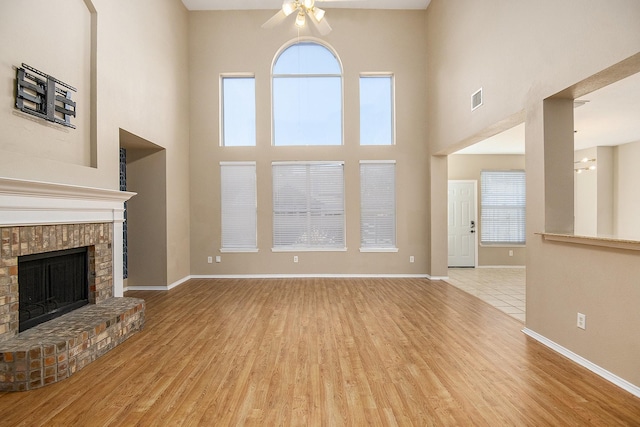 unfurnished living room with ceiling fan, light wood-type flooring, a fireplace, and a towering ceiling