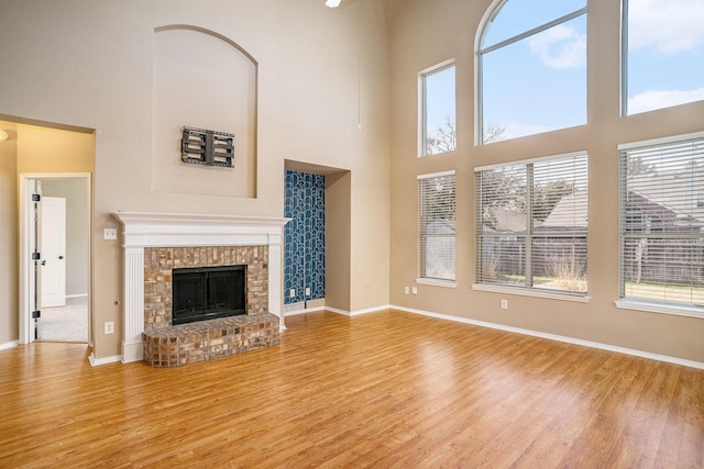 unfurnished living room featuring a high ceiling, a brick fireplace, and light hardwood / wood-style flooring