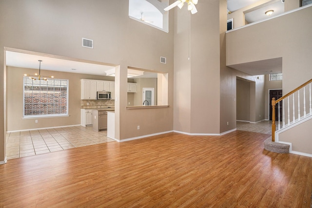 unfurnished living room with ceiling fan with notable chandelier, a healthy amount of sunlight, and light wood-type flooring