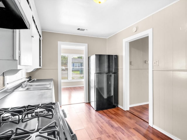 kitchen with hardwood / wood-style floors, black refrigerator, sink, stainless steel gas range, and white cabinetry