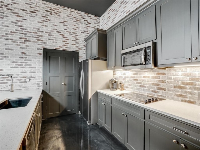 kitchen with sink, light stone counters, brick wall, gray cabinets, and appliances with stainless steel finishes