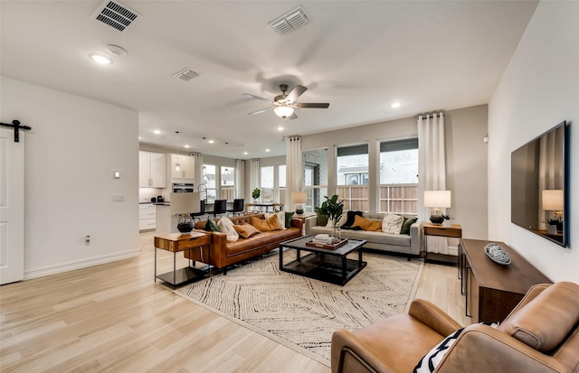 living room featuring a barn door, ceiling fan, sink, and light wood-type flooring