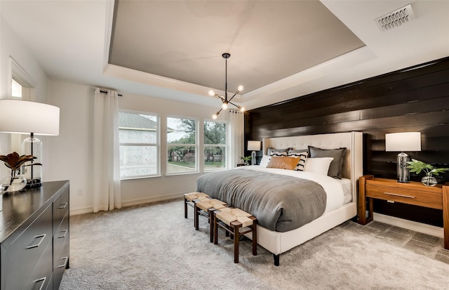 carpeted bedroom featuring a raised ceiling and an inviting chandelier