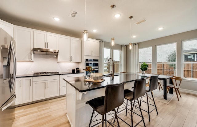 kitchen with appliances with stainless steel finishes, sink, pendant lighting, a center island with sink, and white cabinetry