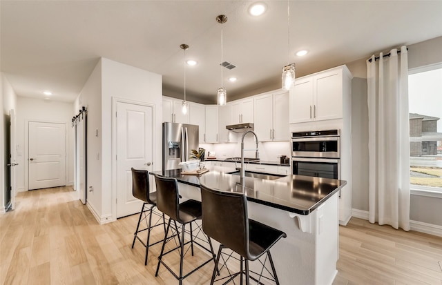 kitchen featuring appliances with stainless steel finishes, light wood-type flooring, a barn door, white cabinets, and an island with sink