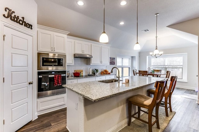 kitchen featuring appliances with stainless steel finishes, vaulted ceiling, white cabinets, light stone counters, and sink