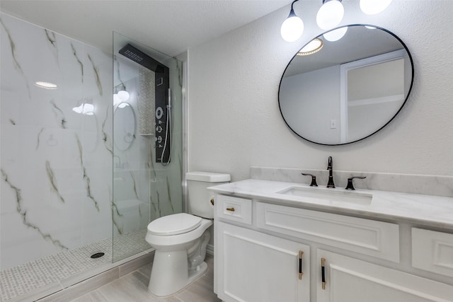 bathroom with a textured wall, toilet, vanity, and a marble finish shower